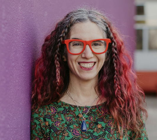 headshot of dana, a white woman with red glasses and red ombre hair